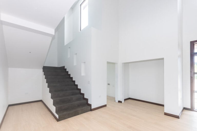 Modern white interior with a staircase featuring dark steps leading to an upper level in a property on Roatan, Honduras.