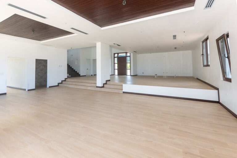 Spacious empty interior of a modern building in Roatan, Honduras, featuring white walls, wooden ceiling accents, and large windows allowing natural light.