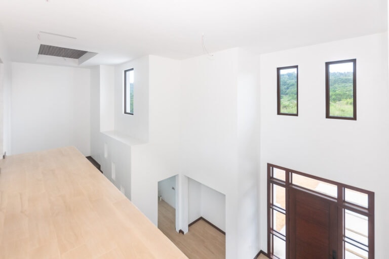 Bright, modern interior of a new house in Roatan, Honduras with white walls, large windows, and high ceilings offering scenic views of lush green landscapes.