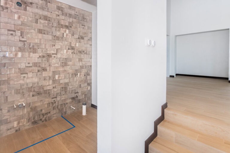 Interior view of an unfinished room in Roatan, Bay Islands, Honduras with a brick accent wall and wooden floors awaiting finishing touches.