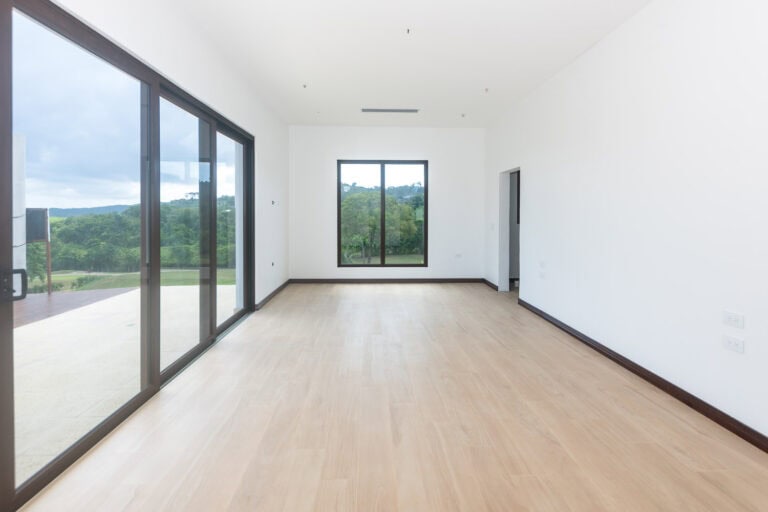 Bright, empty living space with large sliding glass doors and windows showcasing lush green trees and hills of Roatan, Honduras.