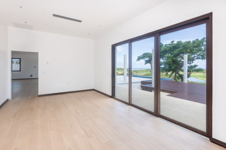Bright interior space in a modern home on Roatan, Honduras, with large sliding glass doors opening to a scenic view of trees, water, and the island landscape.