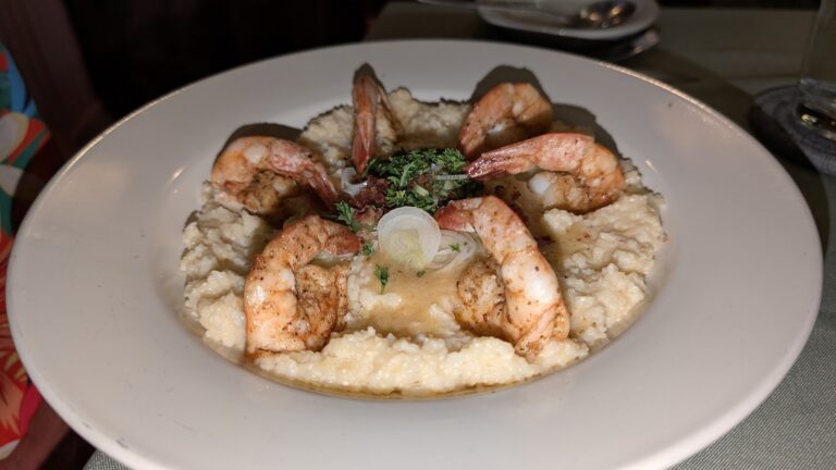 A plate of shrimp and mashed potatoes garnished with fresh herbs, served on a white dish in a restaurant setting on Roatan, Honduras.