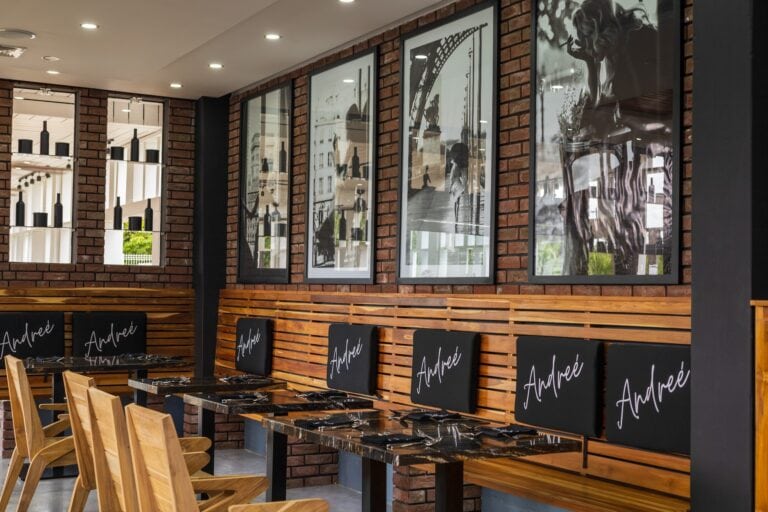 Interior of a restaurant in Roatan, Honduras, featuring wooden chairs, black tables with place settings, black chalkboards with "Andrée" written on them, and framed black-and-white artwork on a brick wall.