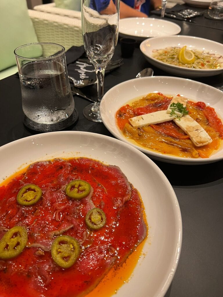Creamy seafood ceviche with lemon slices served in white bowls at a restaurant in Roatan, Honduras, with a dark table setting, glasses of water, and a partially visible person in the background.