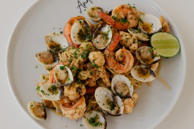 A seafood pasta dish with shrimp, clams, and garnished with chopped parsley and lime wedges, served on a white plate with "Roatan" inscribed on it in Honduras.