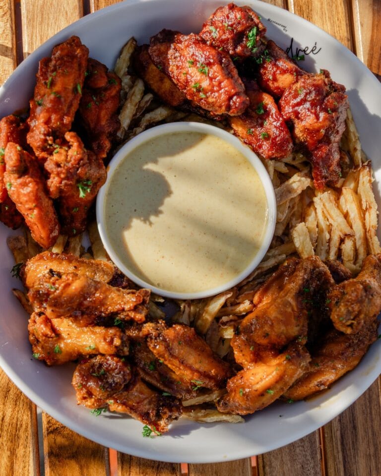 A plate of assorted fried chicken wings with barbecue sauce and a dipping sauce on the side, served on a wooden table in Roatan, Honduras.
