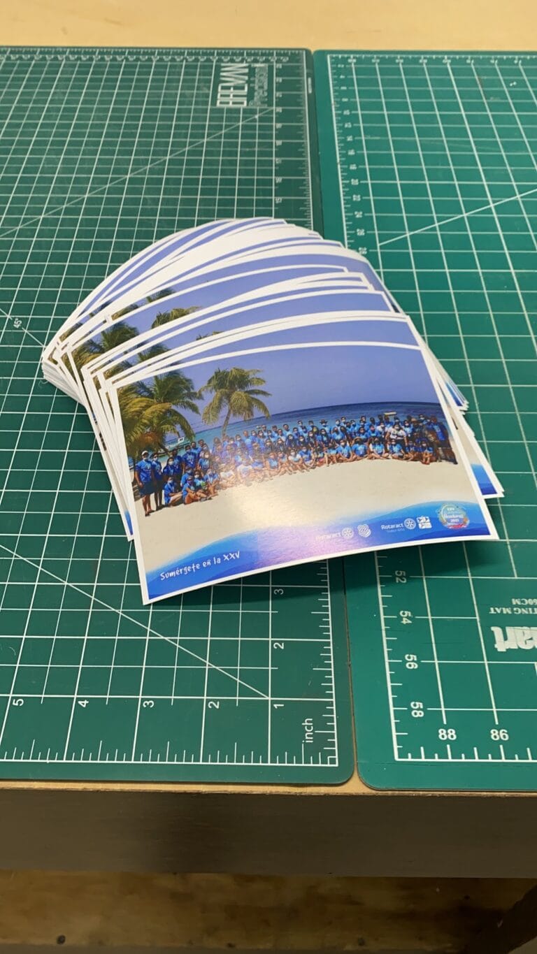 A stack of photographs featuring palm trees, a beach, and a group of people in blue uniforms on a sandy shoreline in Roatan, Honduras.