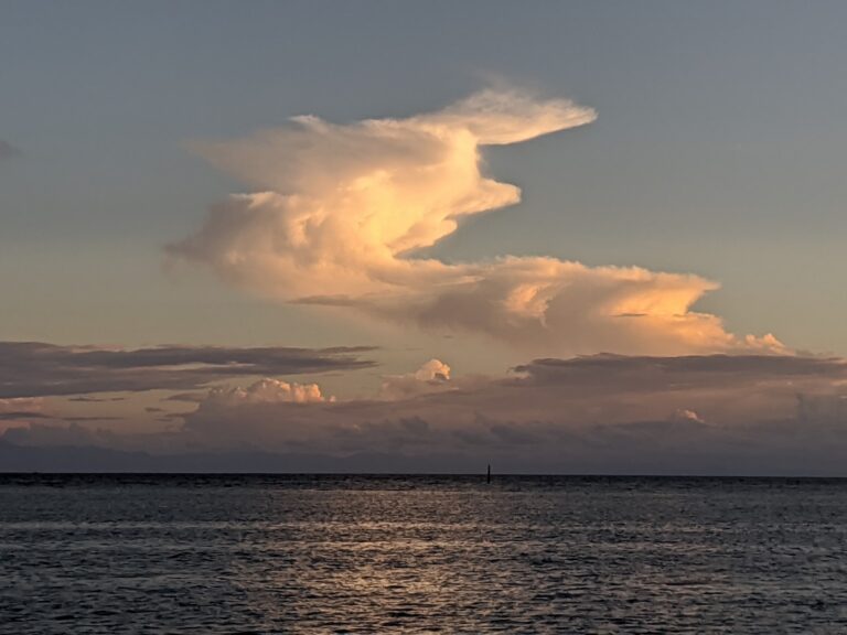 A sunset over the ocean with illuminated clouds and the horizon visible from Roatan, Honduras.