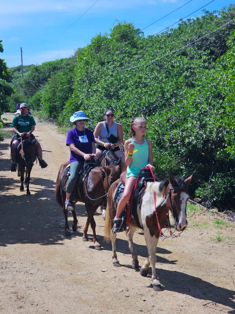 A group of people riding horses along a dirt trail surrounded by lush green vegetation on Roatan, Honduras.