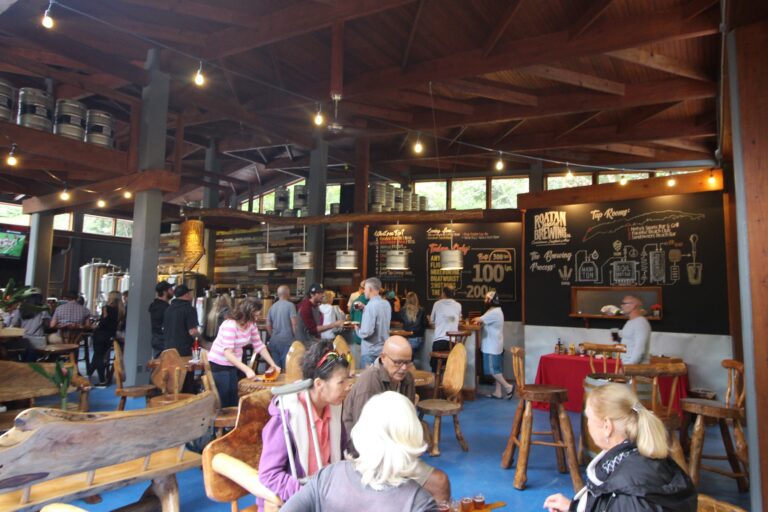 A crowded bar or restaurant in Roatan, Honduras, features wooden decor, large black chalkboard menus, and people enjoying drinks and conversation inside.
