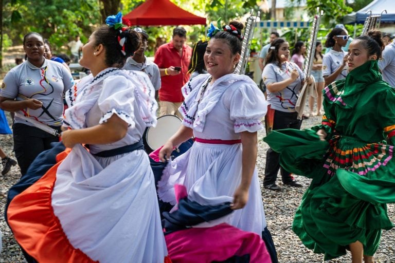 Traditional Honduran dancers in colorful costumes perform during a cultural event in a green outdoor setting on Roatan, Honduras.