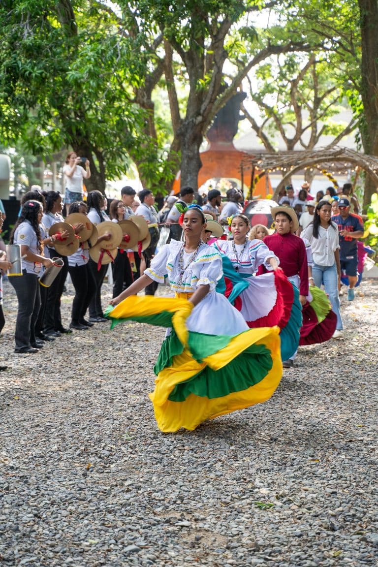 Colorful traditional Honduran dance costumes are worn by women performing a cultural dance in a park surrounded by trees on Roatan, Honduras.