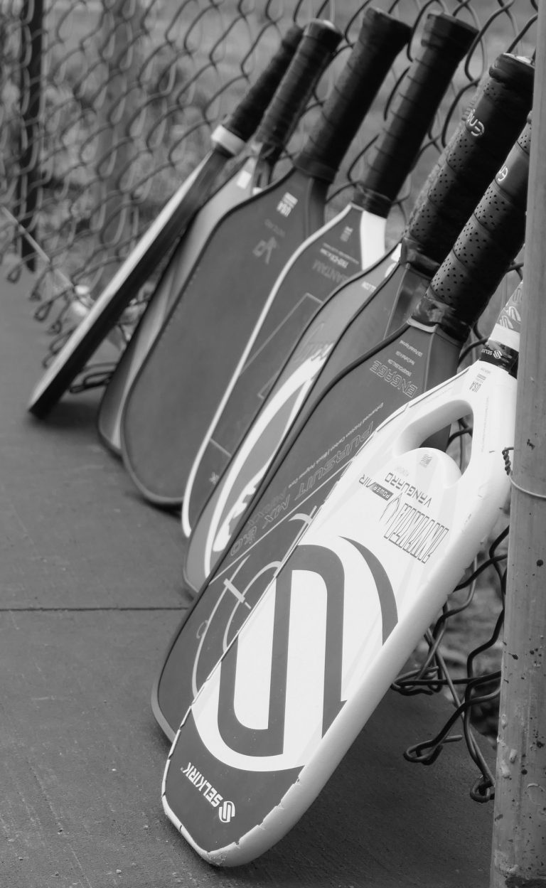 Surfboards with branding and graphics are lined up and leaning against a wire fence on a paved surface in Roatan, Honduras.