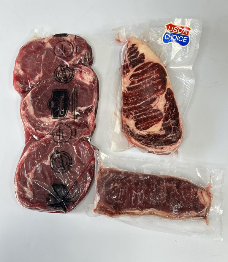 Two vacuum-sealed cuts of raw beef are displayed on a white surface, with one labeled as USDA Choice and the other without visible branding, set against the backdrop of Roatan, Honduras.