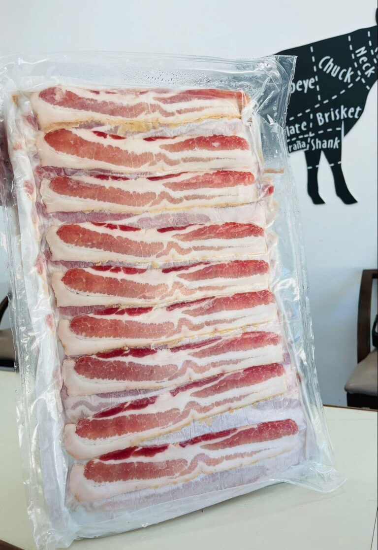 Bundles of raw bacon slices are displayed in vacuum-sealed packaging against a white wall featuring a black silhouette of a pig with labels such as "Roatan" and "Honduras.
