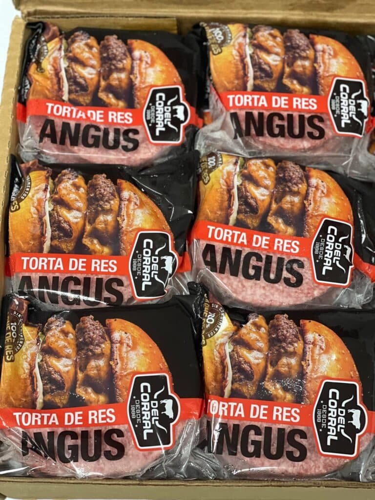 Packages of frozen Angus beef steaks labeled "Torta de Res" are displayed in a wooden box, with the packaging indicating they are available in Roatan, Honduras.