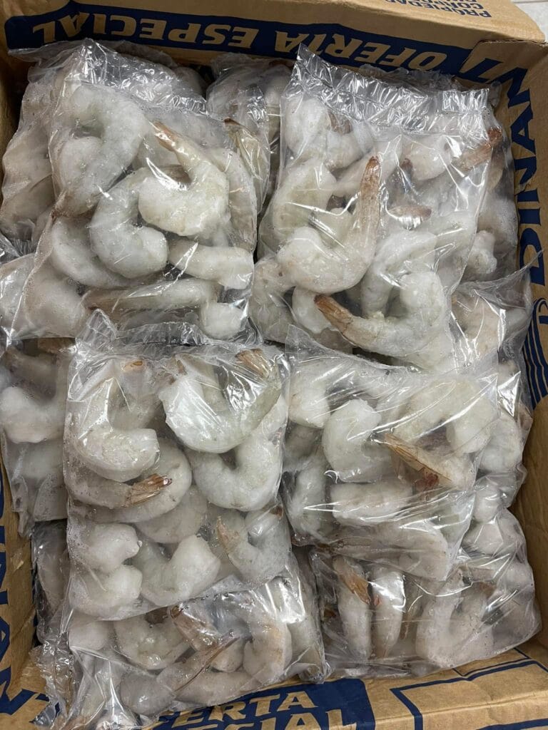 Frozen shrimp packaged in clear plastic bags inside a cardboard box with "Roatan" and "Honduras" labels, set against a neutral background.