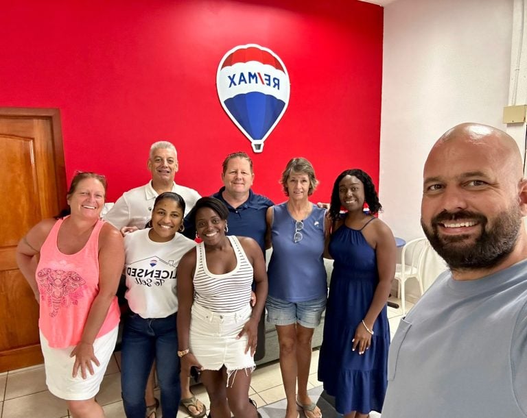 A group of diverse people posing together in front of a red wall with a Roatan and Honduras-themed hot air balloon logo at a business in Roatan, Bay Islands, Honduras.