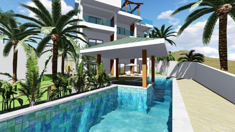 A modern multi-story building with balconies surrounded by palm trees and lush greenery features a private swimming pool with a shaded lounge area and lounge chairs, set against a backdrop of clear blue skies on Roatan, Honduras.