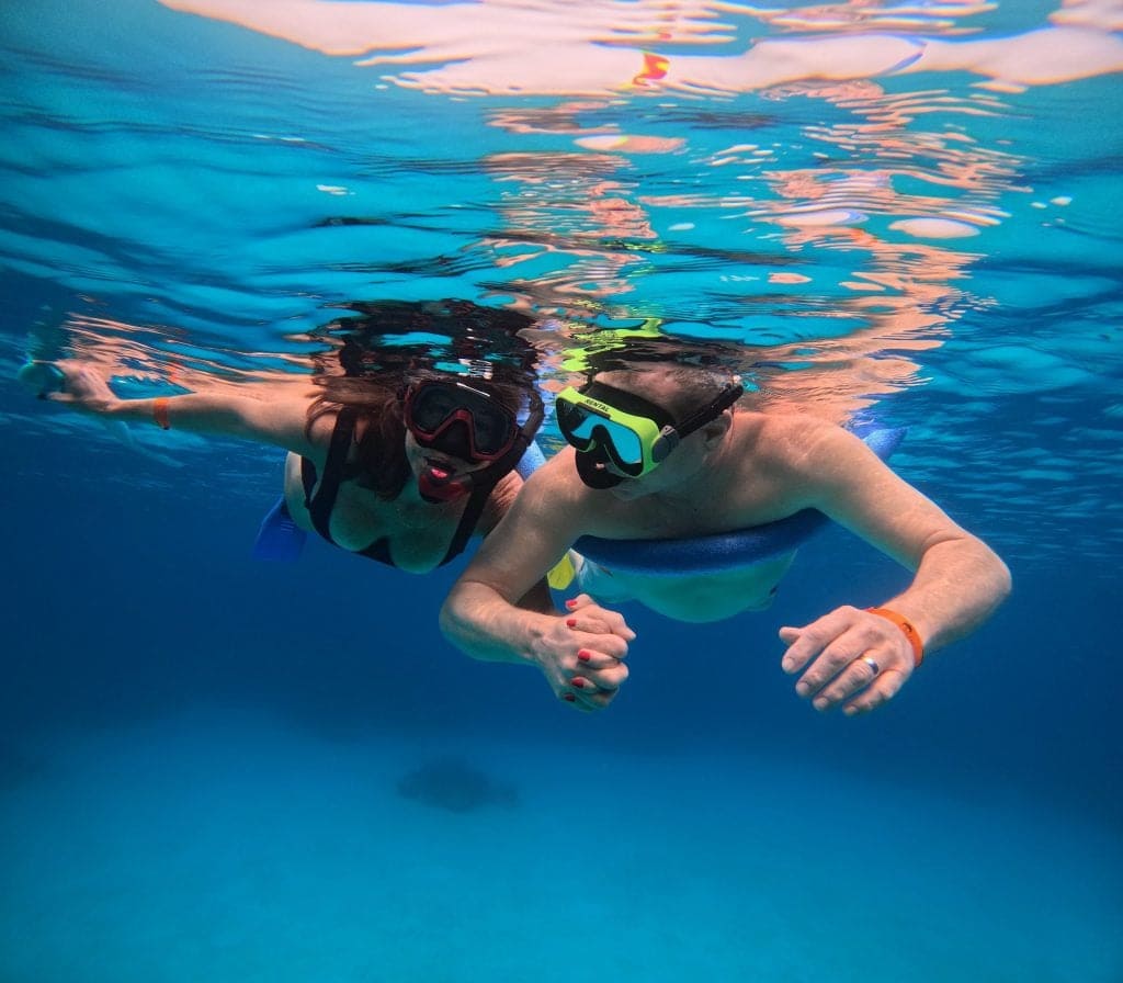 A person wearing snorkeling gear floats underwater near the surface in the clear blue waters of Roatan, Honduras.