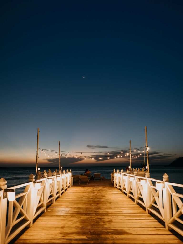 Pier at sunset with string lights and a crescent moon over the Caribbean Sea in Roatan.