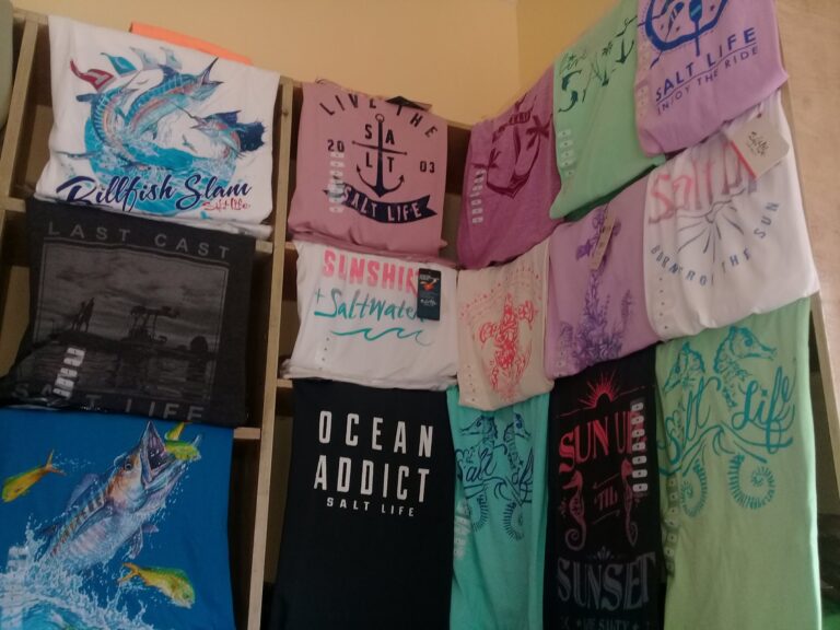 Colorful beach towels with marine-themed and motivational designs are displayed on a wooden rack in a shop on Roatan, Bay Islands, Honduras.