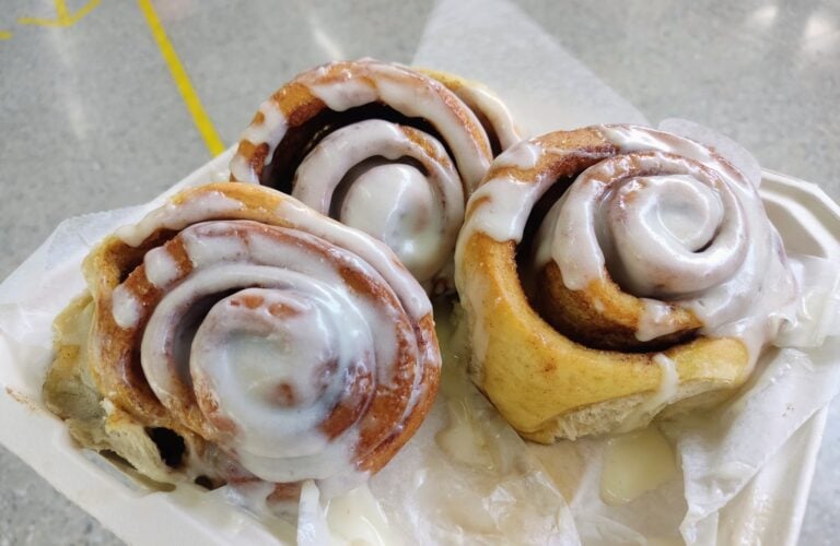 Cinnamon rolls with icing are displayed on a paper-lined tray in this image from Roatan, Honduras.