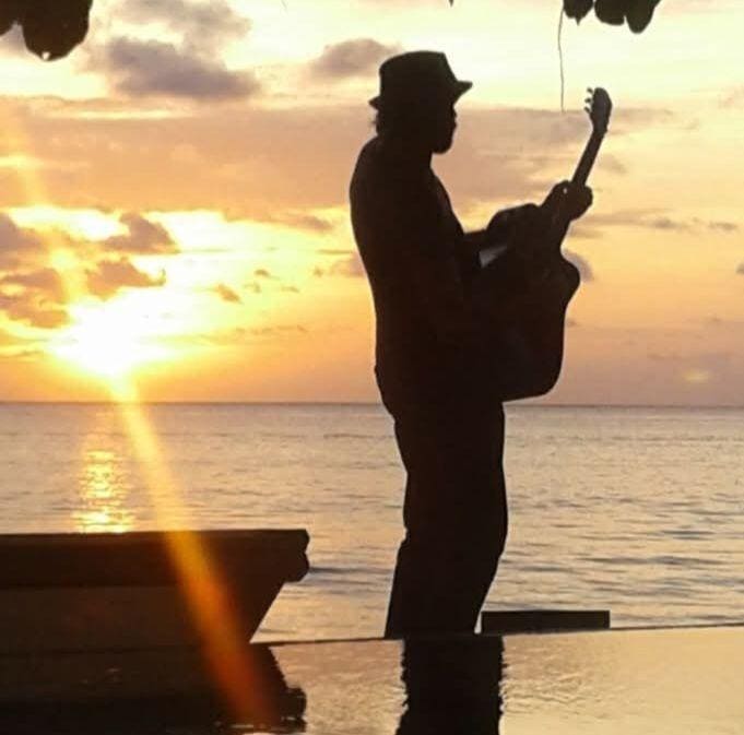 A silhouette of a person playing an acoustic guitar on the beach during a vibrant sunset in Roatan, Honduras, with the ocean and colorful sky in the background.