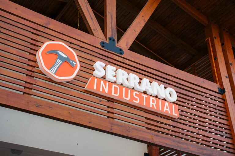 A wooden building in Roatan, Honduras, features a sign for Serrano Industrial, with a logo of a hammer and a wrench on an orange background, indicating an industrial or hardware business.