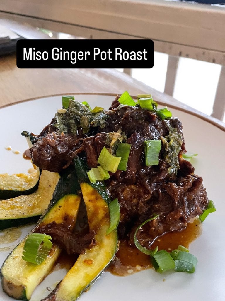 A plated dish featuring tender meat, grilled zucchini and yellow squash, topped with chopped green onions, served with a lemon wedge, in a restaurant setting on Roatan, Honduras.