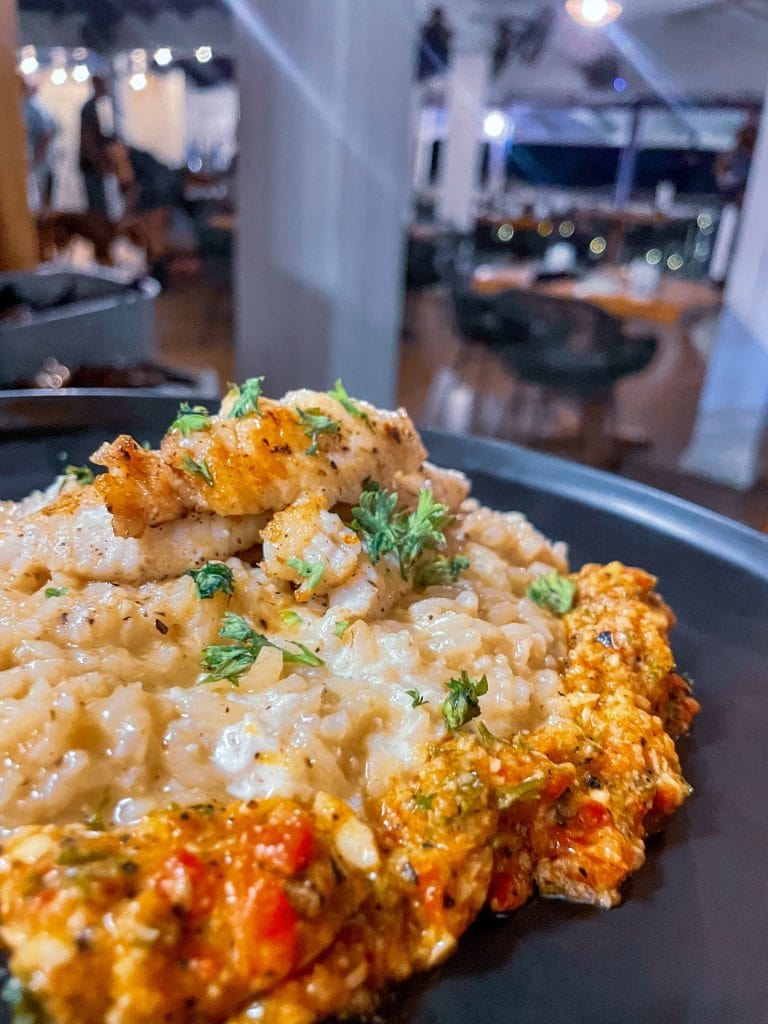 A close-up of a plate of creamy seafood pasta garnished with fresh herbs, set inside a restaurant on Roatan, Honduras, with blurred interior dining area and seating visible in the background.