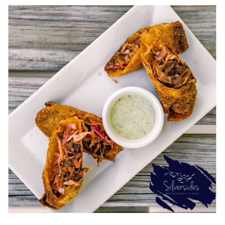 Fried empanadas filled with shredded meat and vegetables served with a creamy dipping sauce on a white rectangular plate in a Roatan, Honduras restaurant.