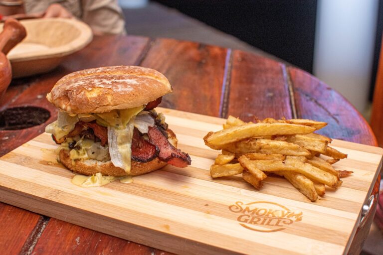 A bacon, egg, and cheese sandwich with crispy French fries served on a wooden tray at a restaurant in Roatan, Honduras.