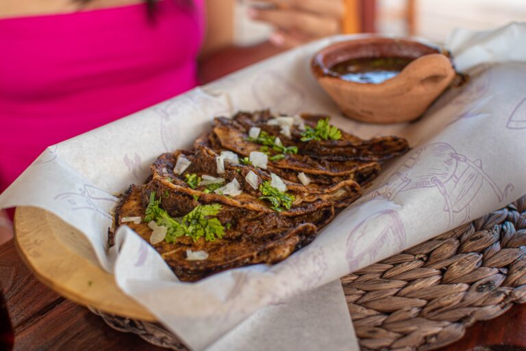 Grilled meat tacos topped with chopped onions and cilantro served with a side of salsa in a basket on a table in Roatan, Honduras.