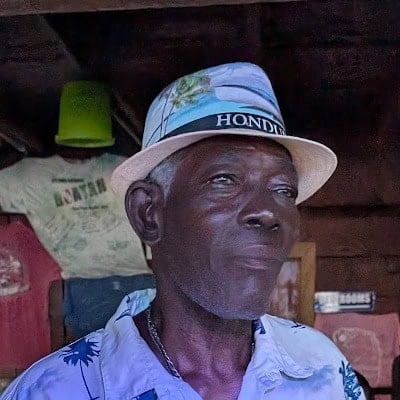 Elderly man wearing a hat in a rustic setting in Roatan.
