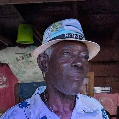 Elderly man wearing a hat in a rustic setting in Roatan.