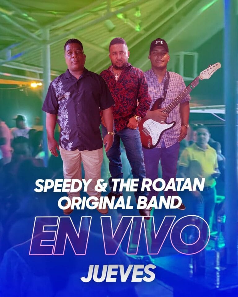 Three men, one holding an electric guitar, perform on stage under colorful lighting at a music event in Roatan, Honduras, with an audience visible in the background.
