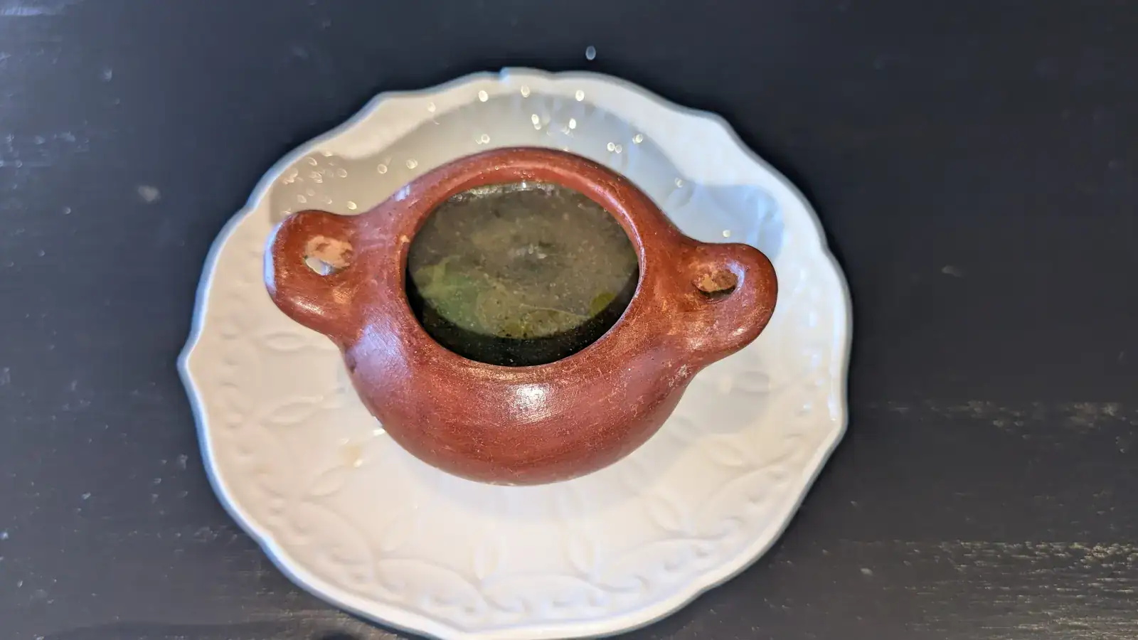 Small traditional Honduran clay cup with liquid, placed on a white decorative plate on a dark surface in Roatan, Honduras.