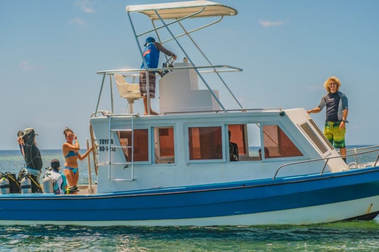 A group of people on a boat in Roatan, Honduras, preparing for diving or snorkeling activities with scuba tanks on the deck under a clear blue sky.