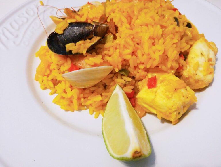 A plate of vibrant yellow rice with seafood, lemon wedges, and fresh vegetables served on a white plate in Roatan, Honduras.