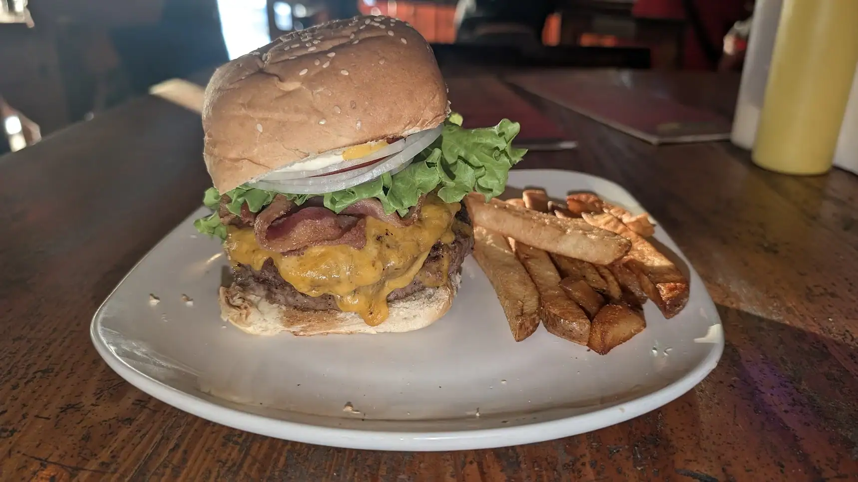 A large cheeseburger with bacon, lettuce, onions, and melted cheese served alongside crispy French fries on a white plate at a restaurant in Roatan, Honduras.