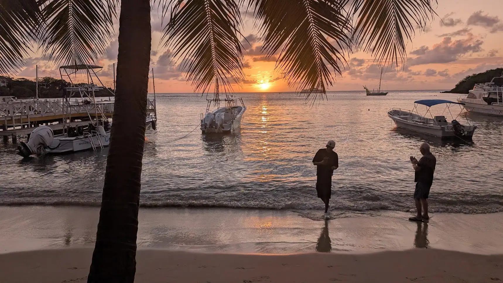 Palm-framed sunset over Half Moon Bay viewed from Sundowners Beach Bar West End Roatan