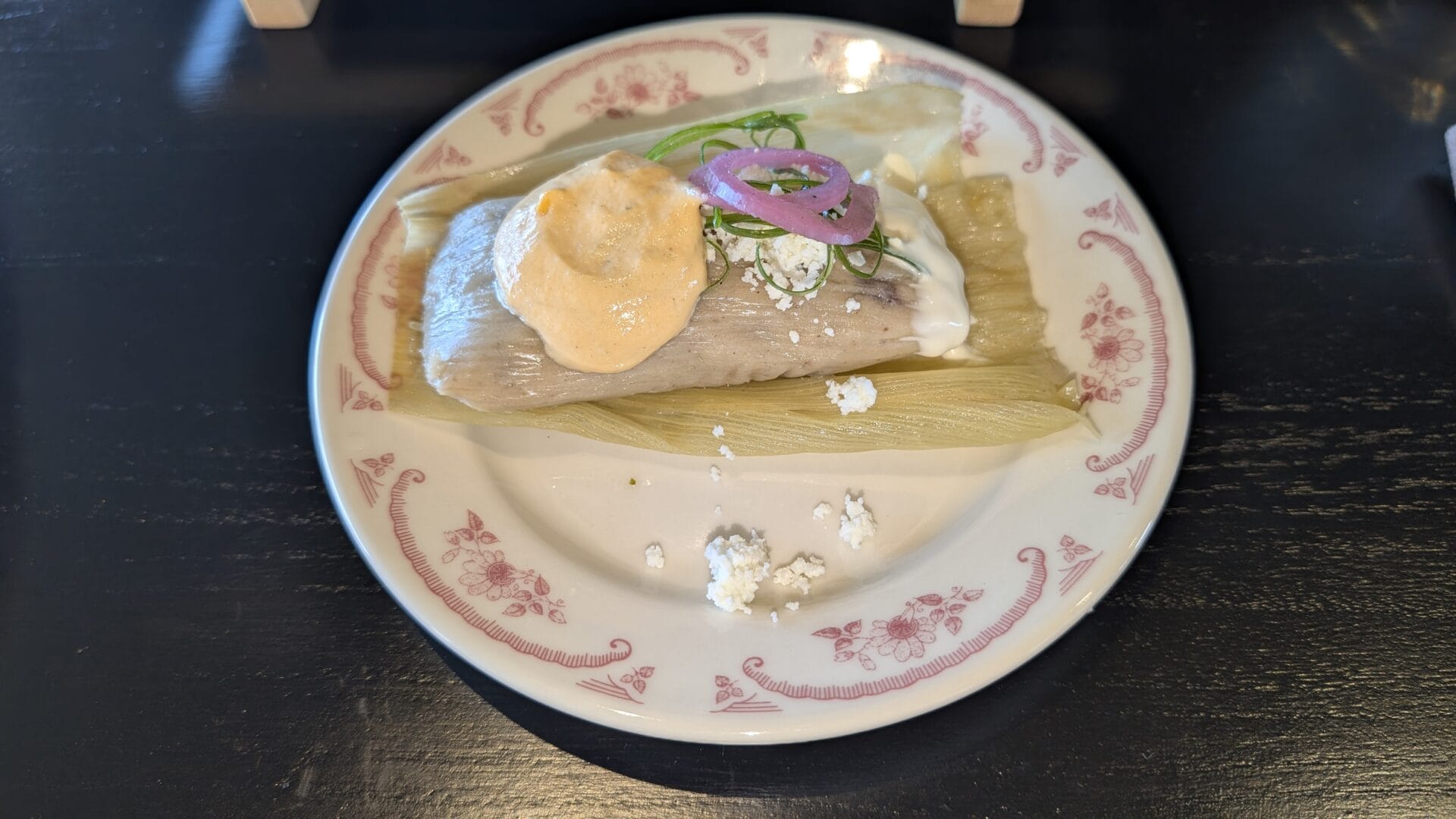 Roatan Honduras traditional dish with tamale-like food topped with sauce, garnished with green onions and pickled red onions on a decorative white plate.