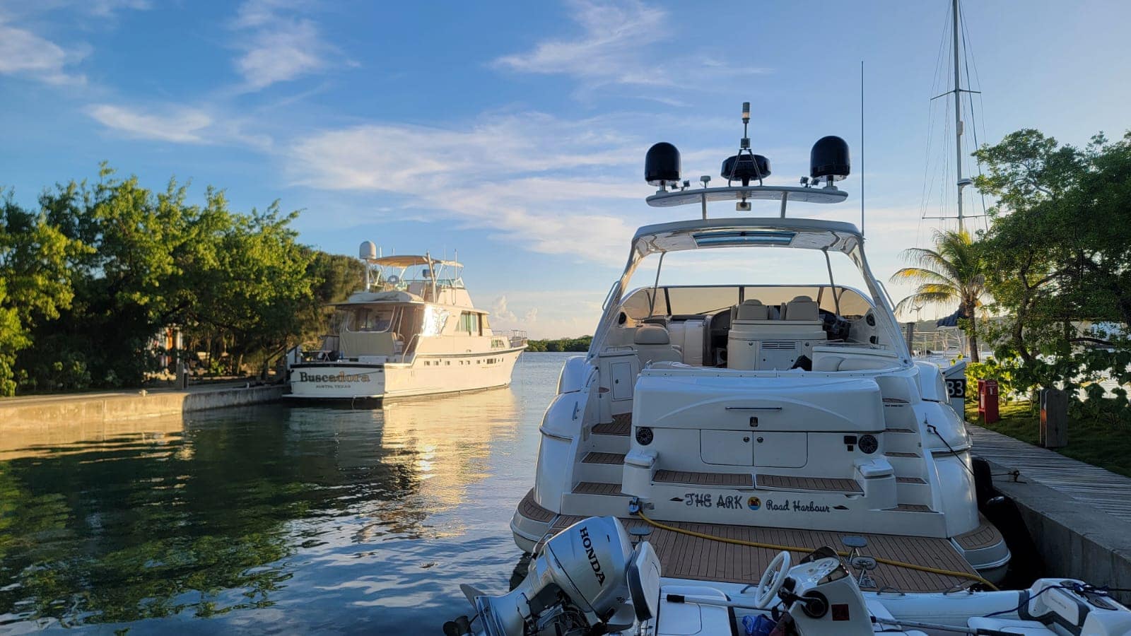 Empty boats docked along a canal in Roatan, Honduras, with lush green trees on the shore and a clear blue sky overhead.