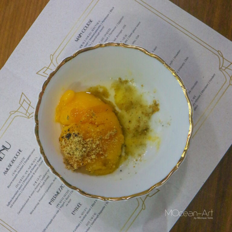 A bowl of yellow mango and chili, garnished with ground spices, placed on a business menu with gold trim details, sitting on a wooden table at a restaurant in Roatan, Honduras.