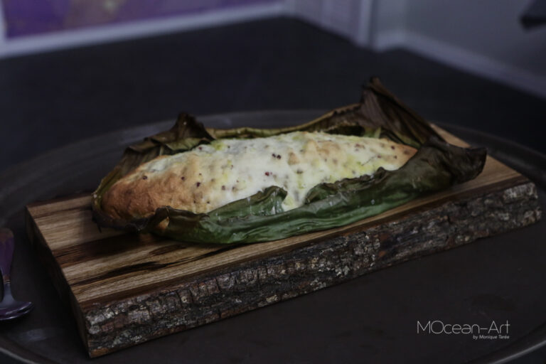 A stuffed and baked banana leaf dish served on a wooden plank at a restaurant in Roatan, Honduras, with melted cheese visible on top.