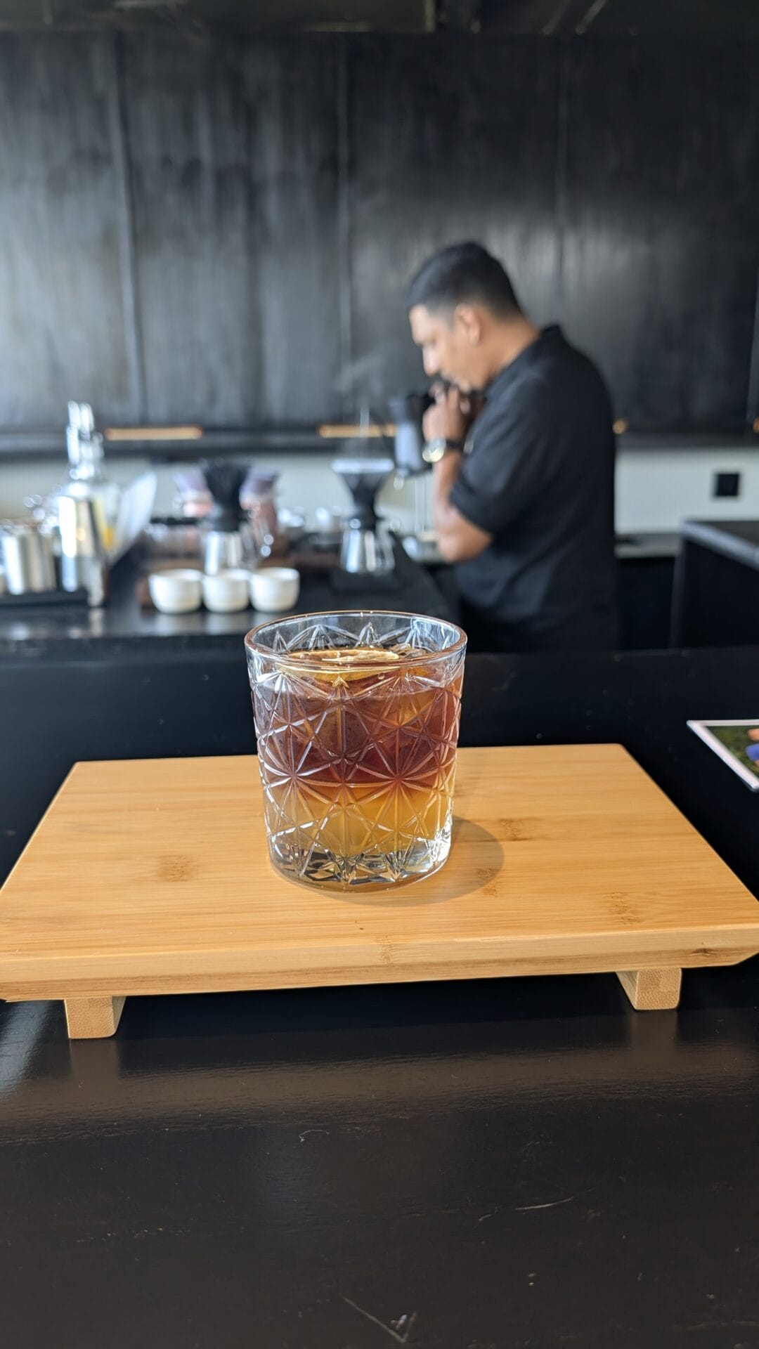 A bartender preparing coffee behind a dark bar counter in Roatan, Honduras, with coffee brewing equipment visible in the background.