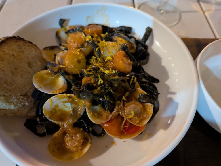 A bowl of seafood stew with shrimp, scallops, and vegetables, garnished with lemon zest, on a white plate at a restaurant in Roatan, Honduras.