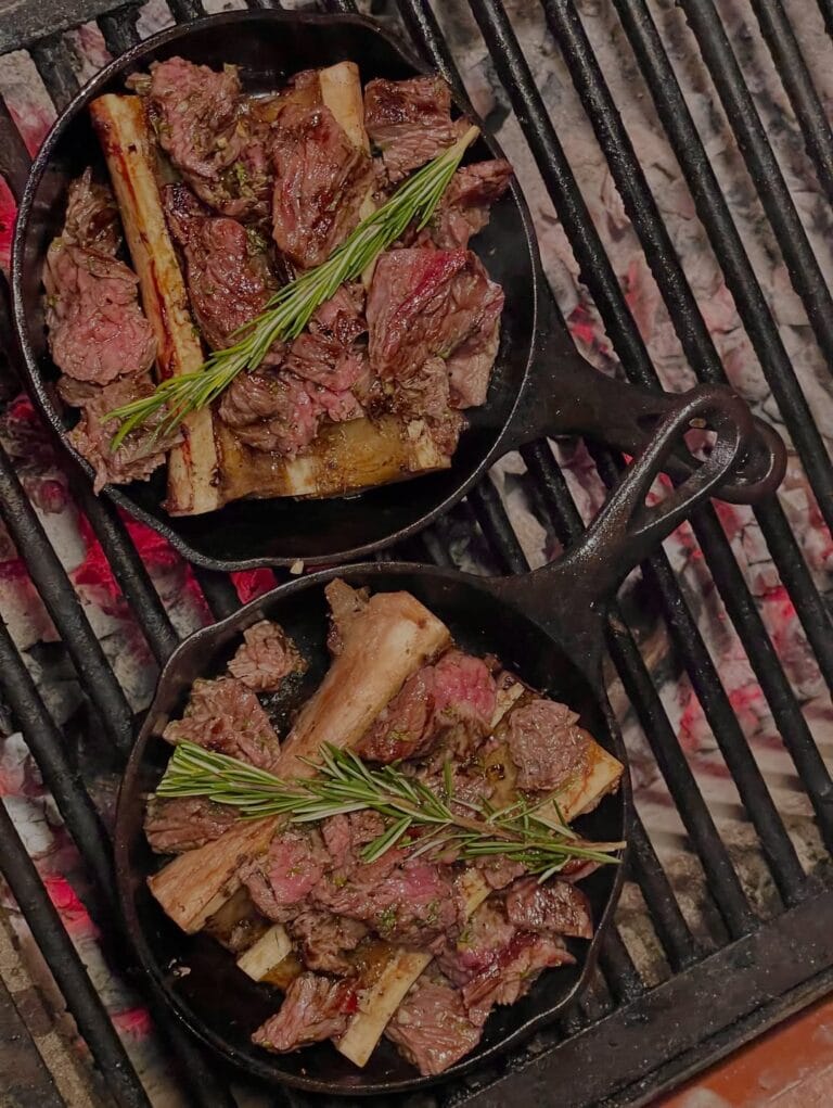 Delicious beef ribs grilling on a barbecue with fresh rosemary sprigs. Perfect for a flavorful Carib.